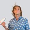 Automatic cover art: Dylan Hand in front of a white background wearing a blue button up shirt covered in swans, holding a hair dryer in his right hand which is blowing his hair up.