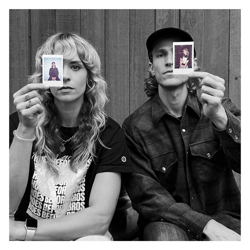 Black and white photo of Haley Johnsen and Dylan Hand holding color poloroid pictures of each other in front of a wooden background